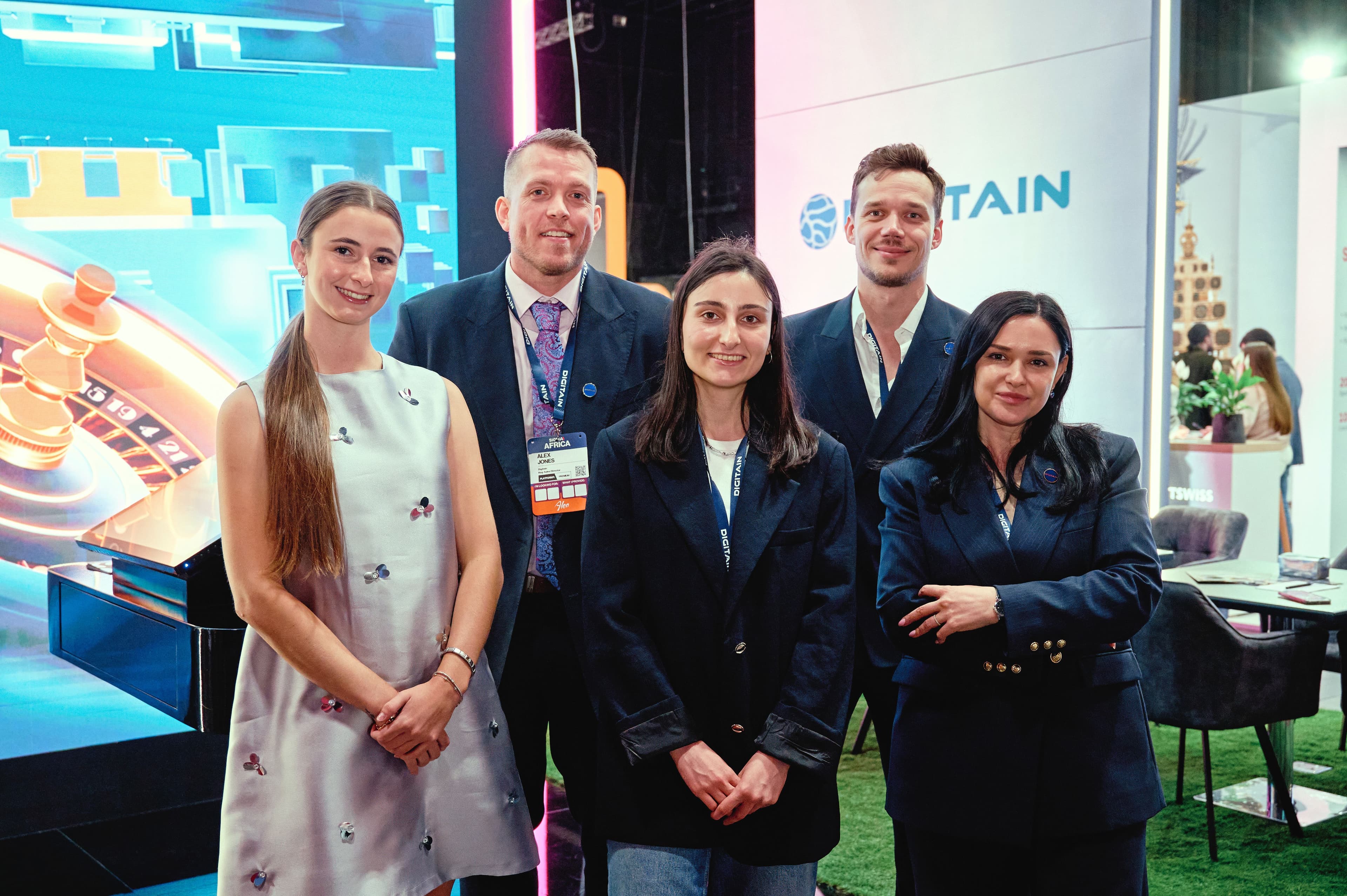 Five smiling professionals, three women and two men, stand at a conference booth.
