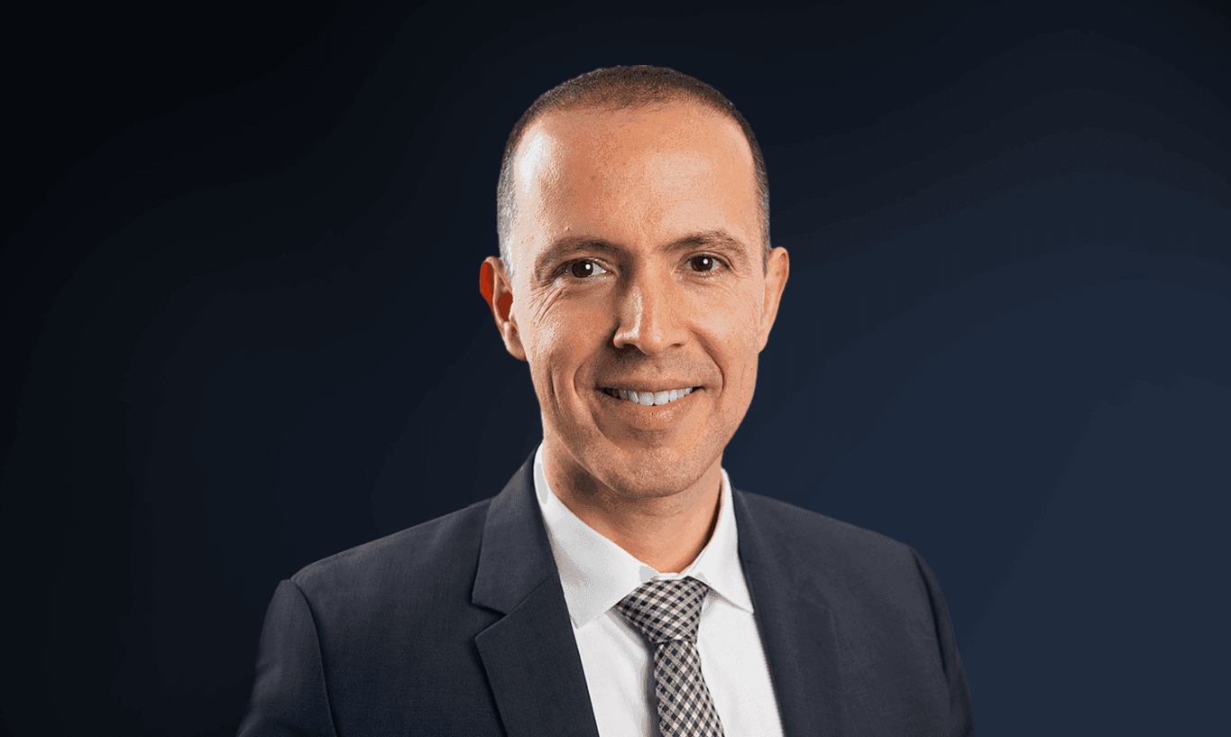 Professional man in a dark suit and patterned tie smiling confidently.
